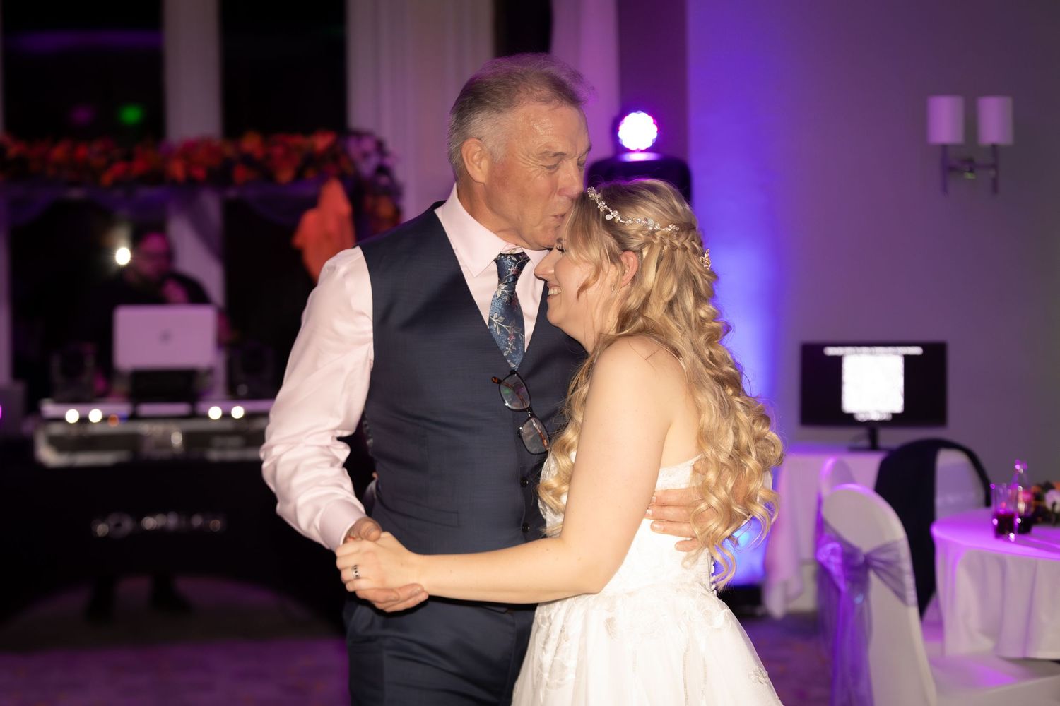 Bride and groom share a romantic first dance at their wedding reception with purple uplighting.