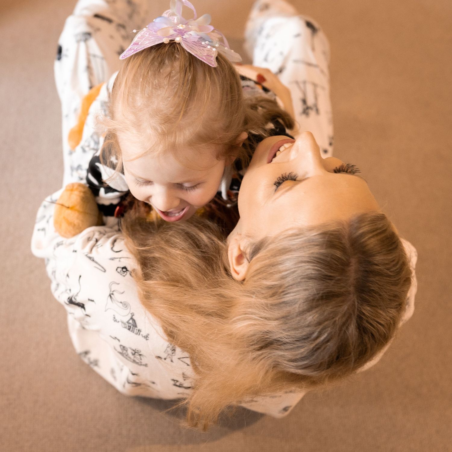 Mother and young daughter in matching pajamas laugh together while lying on the floor, viewed from above.