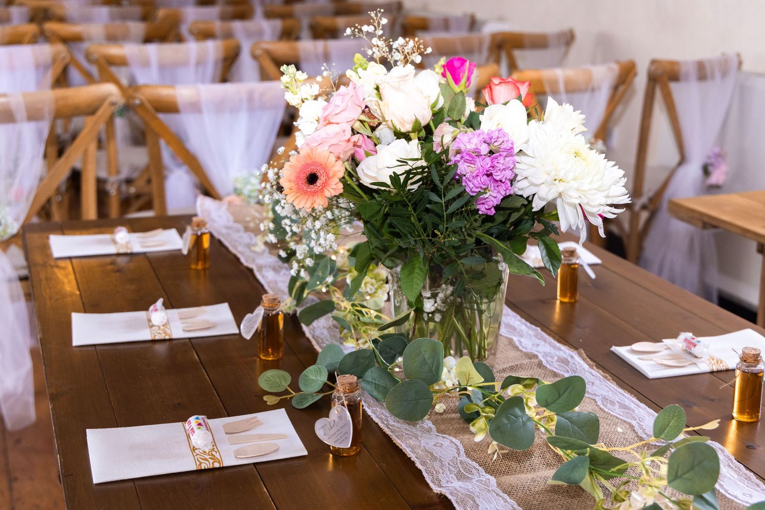 Elegant wedding reception table with colorful floral centerpiece and lace runner in bright venue.