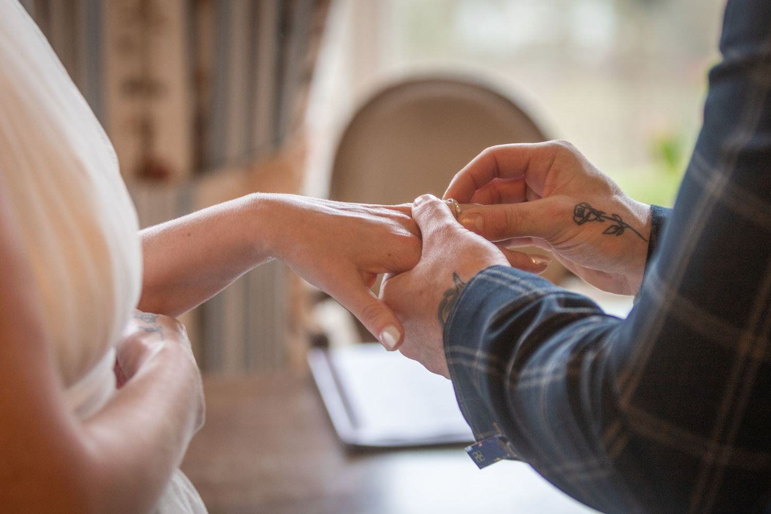 Groom with tattoos placing a wedding ring on bride's finger during ceremony.