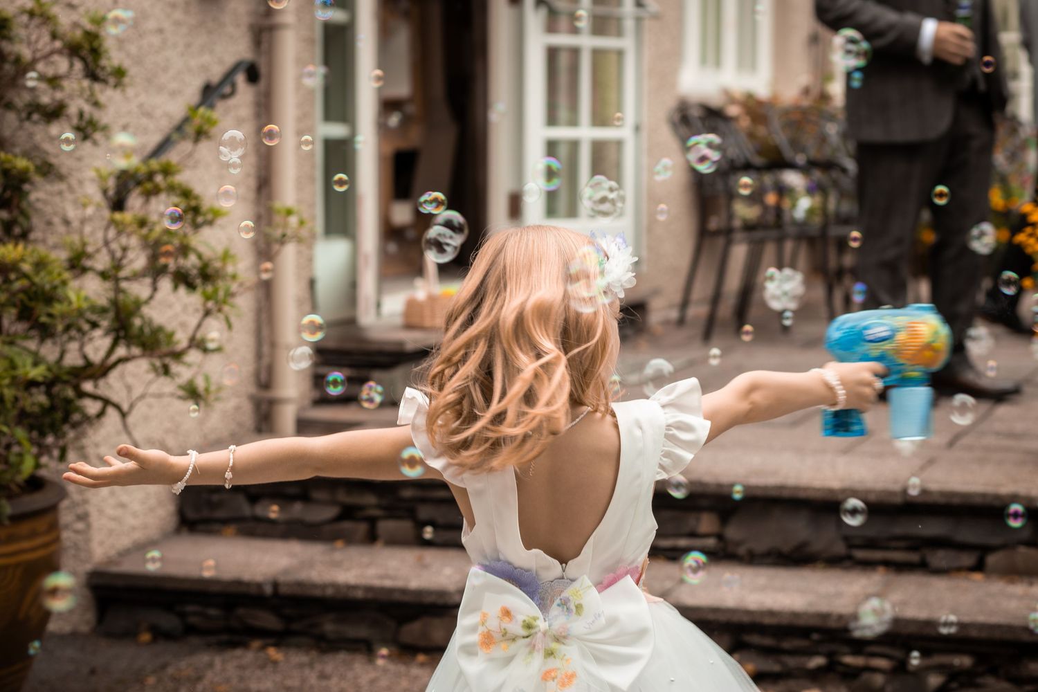 Flower girl twirling with arms outstretched surrounded by floating bubbles at a wedding.