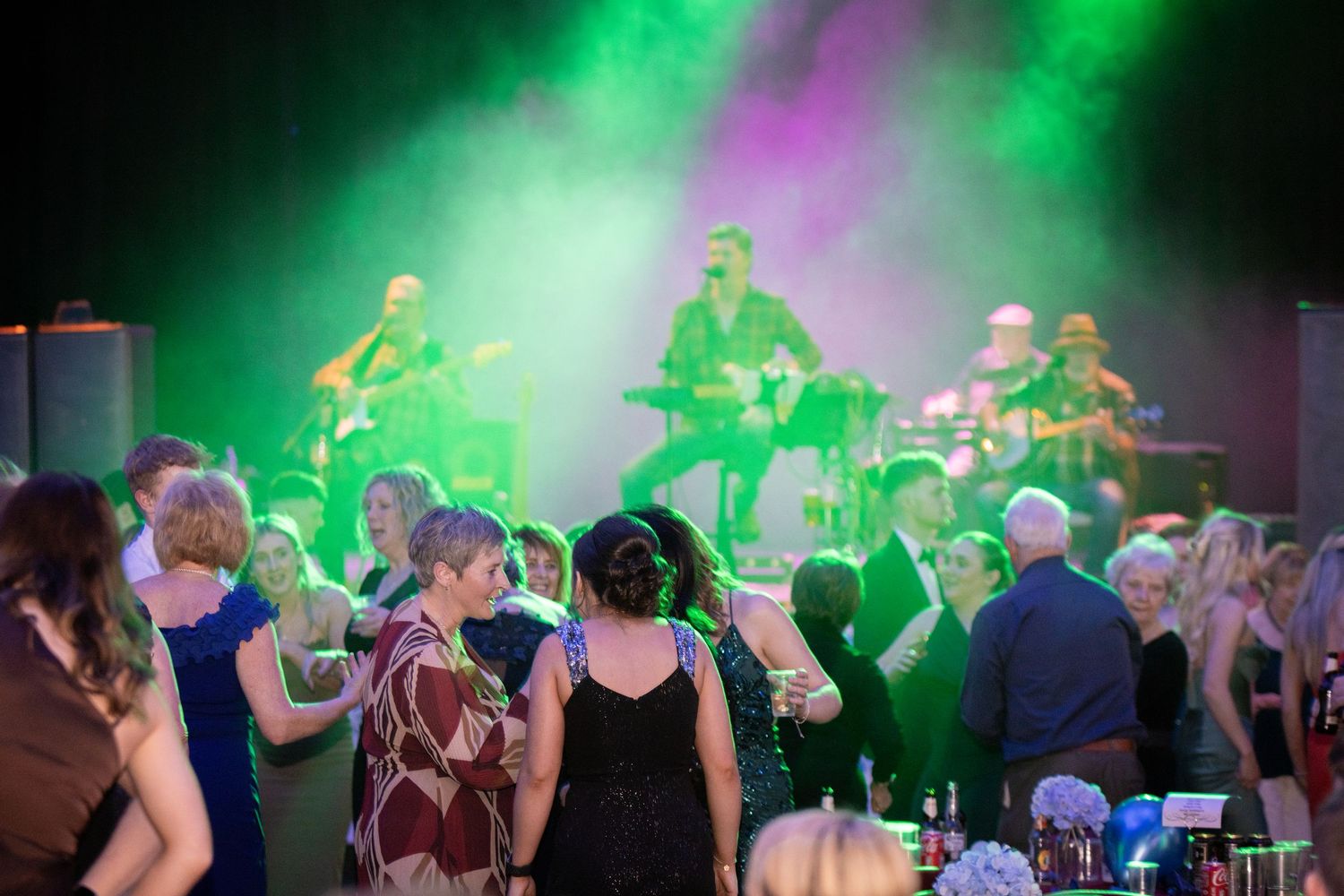 Guests dancing at an elegant evening event with a live band performing under green stage lighting.