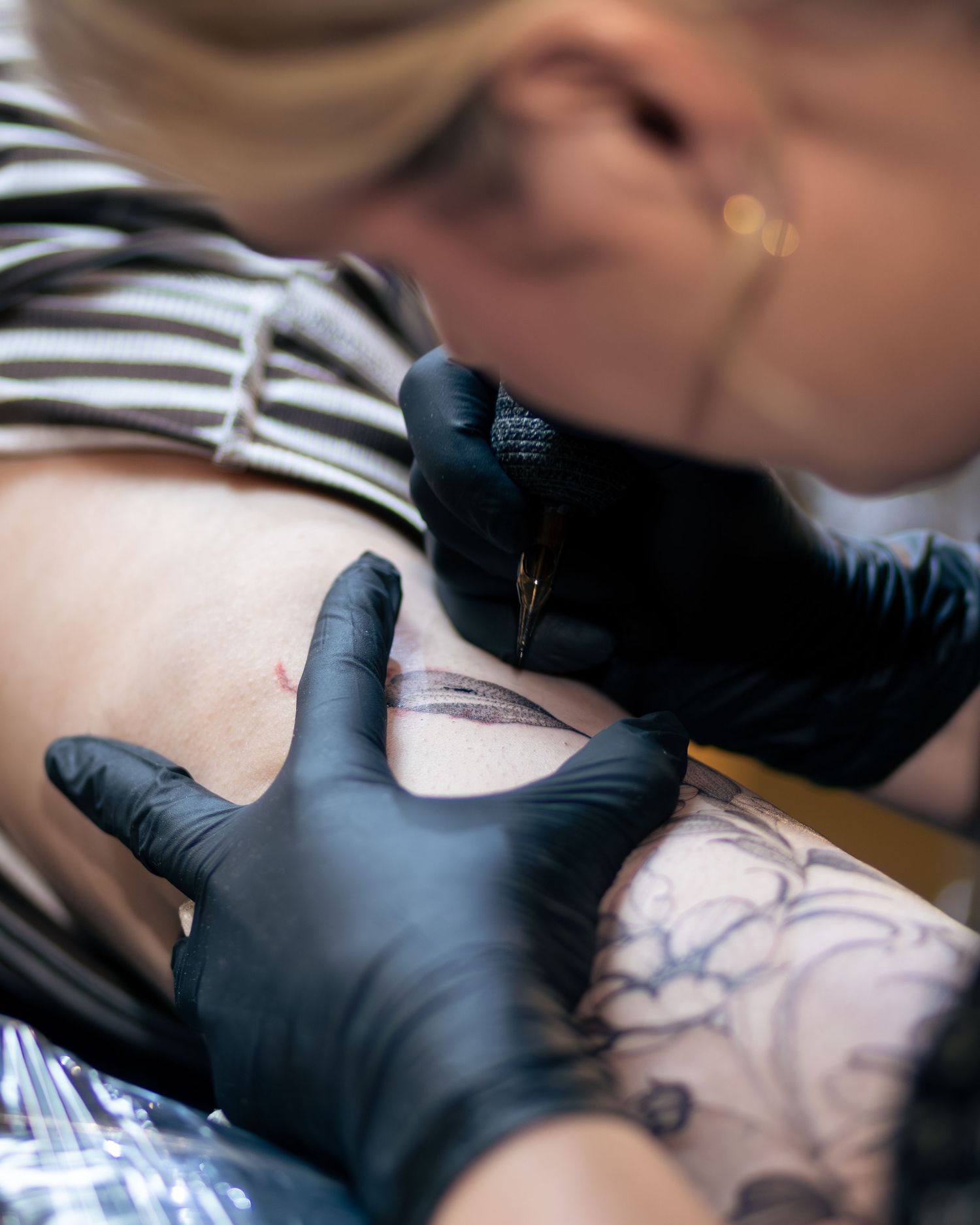 Close-up of tattoo artist using needle to create detailed line work on client's skin.