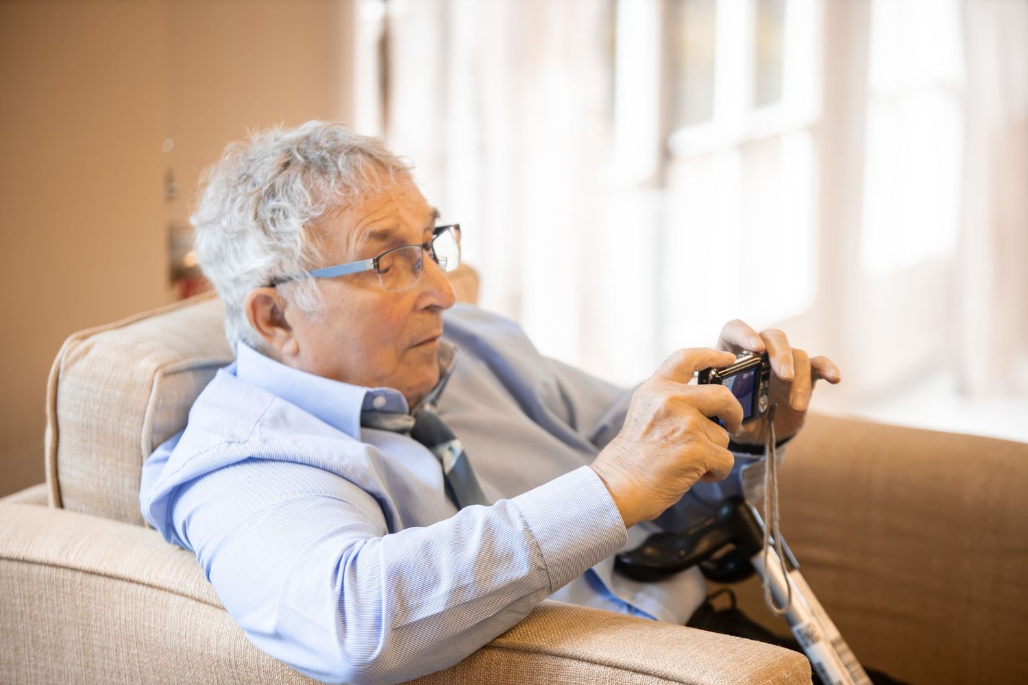 Elderly man with glasses sitting in armchair playing video games with a game controller.