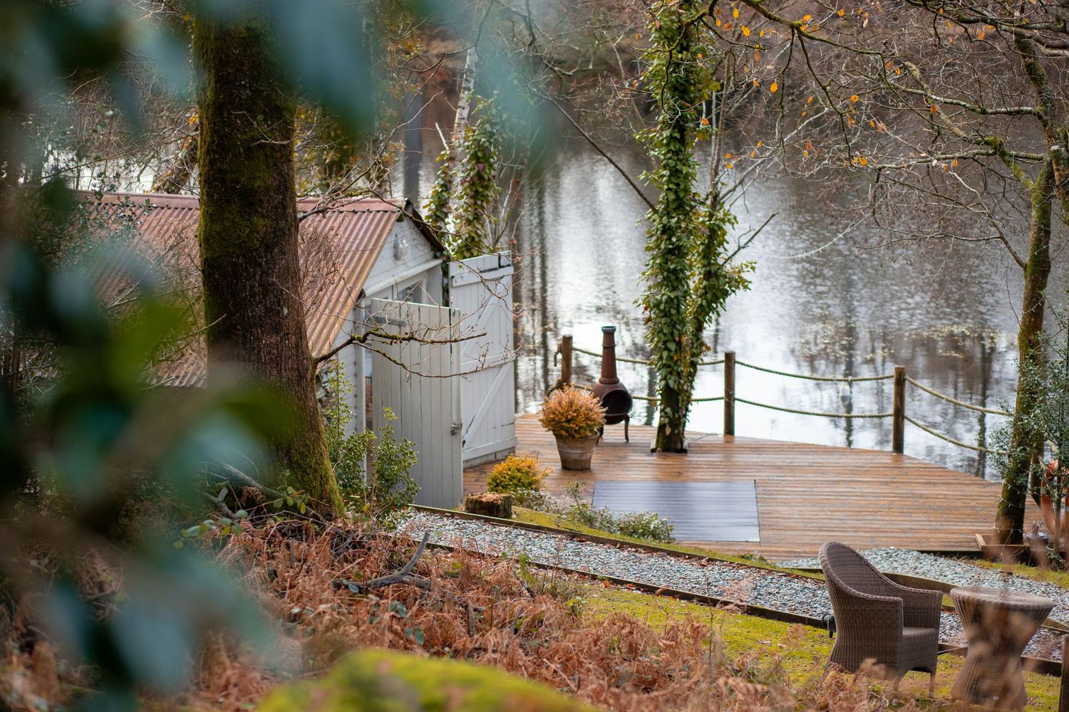 A serene wooden deck overlooking a misty river, surrounded by ivy-covered trees and lush greenery in autumn.