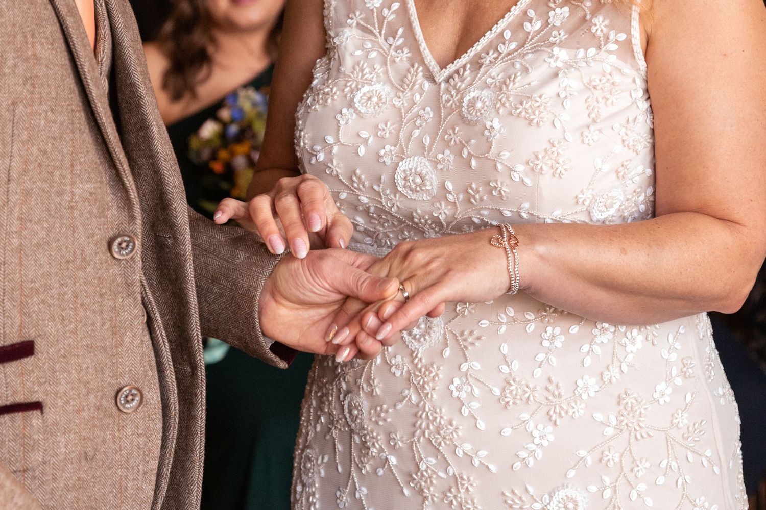 Bride in beaded white gown exchanging rings with partner during wedding ceremony.