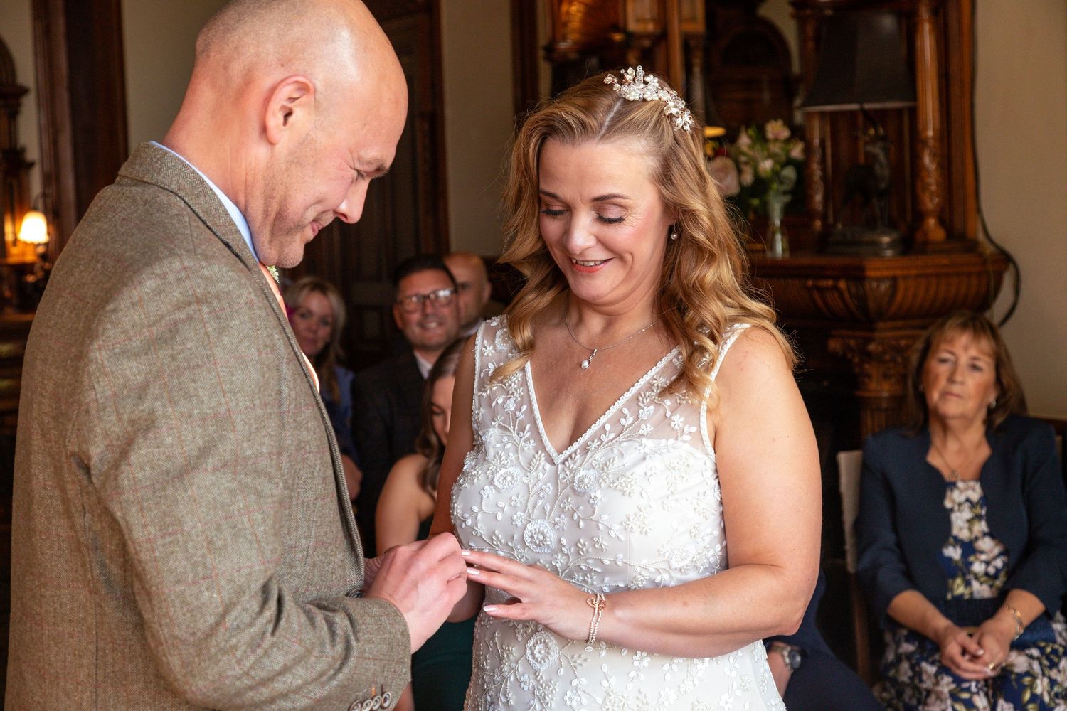 A groom places a wedding ring on his brides finger during an intimate indoor ceremony.