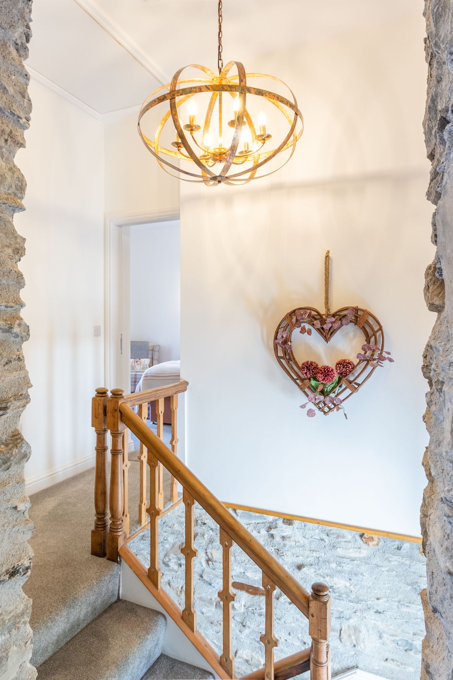 Elegant staircase hallway with exposed stone walls, wooden banister, globe chandelier, and heart wreath decor.