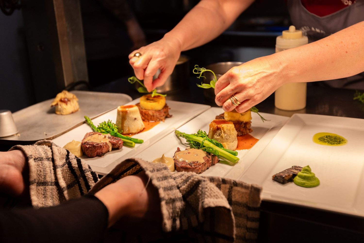 Chefs carefully garnishing multiple gourmet plates with steak and asparagus.