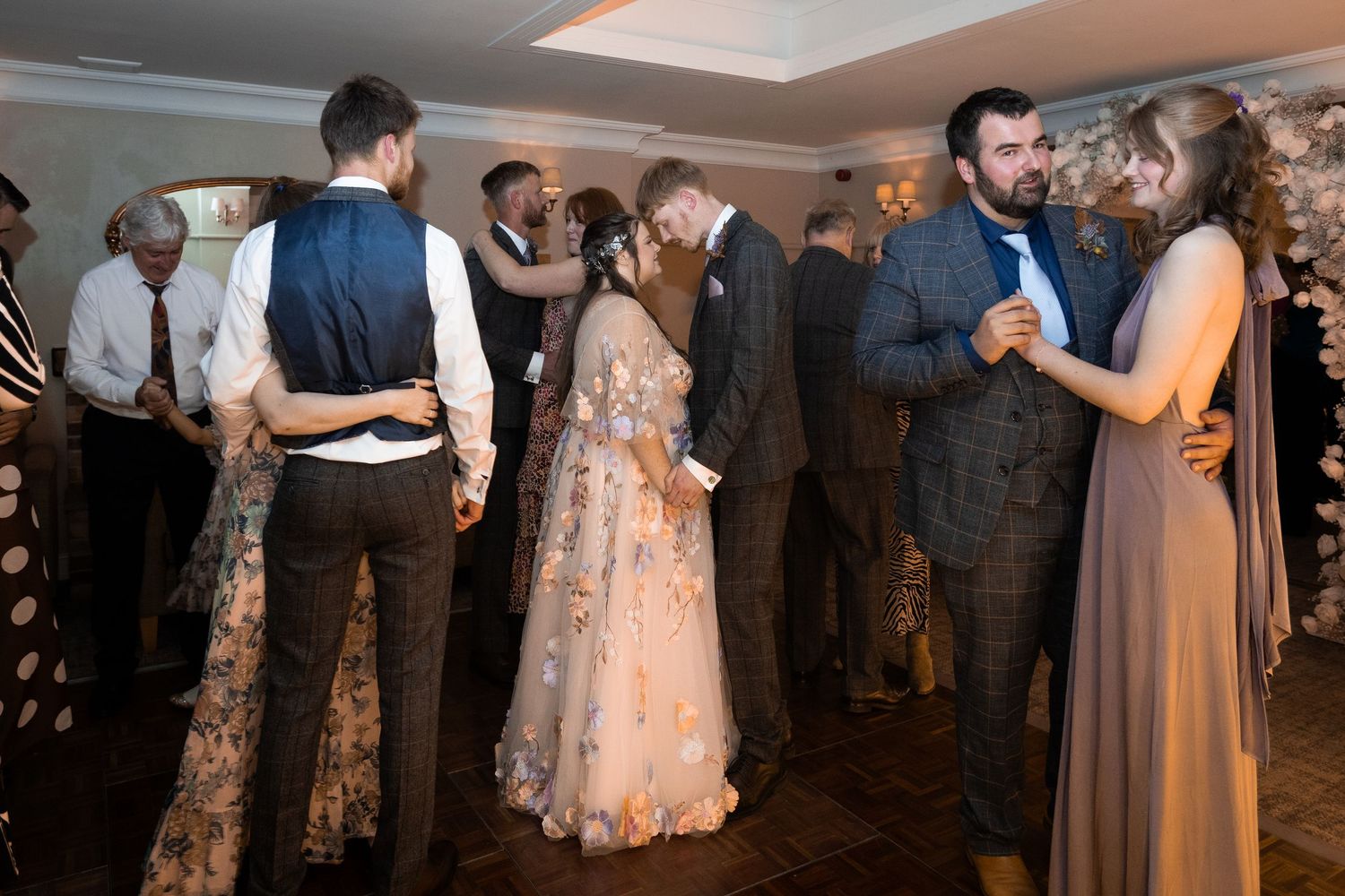 Couples dancing together at an elegant wedding reception in a warmly lit venue.
