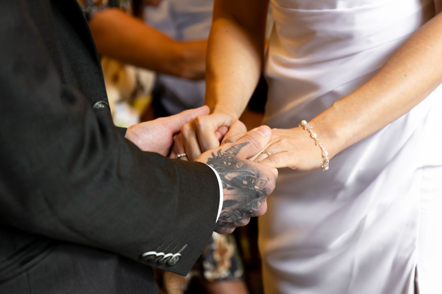 Couple exchanging wedding rings, groom with tattooed hand placing ring on bride's finger during ceremony.