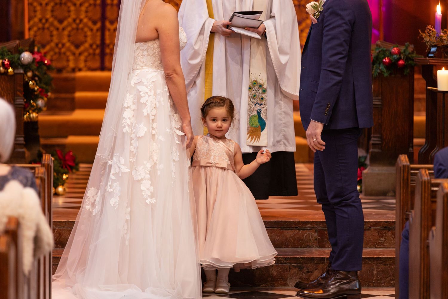 Adorable flower girl stands between bride and groom during a beautiful church wedding ceremony.