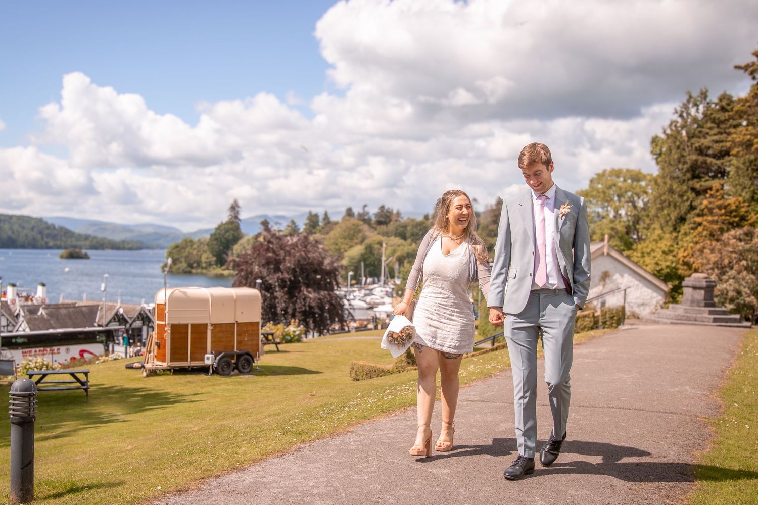 Couple walking hand in hand along a lakeside path on their wedding day in the Lake District.