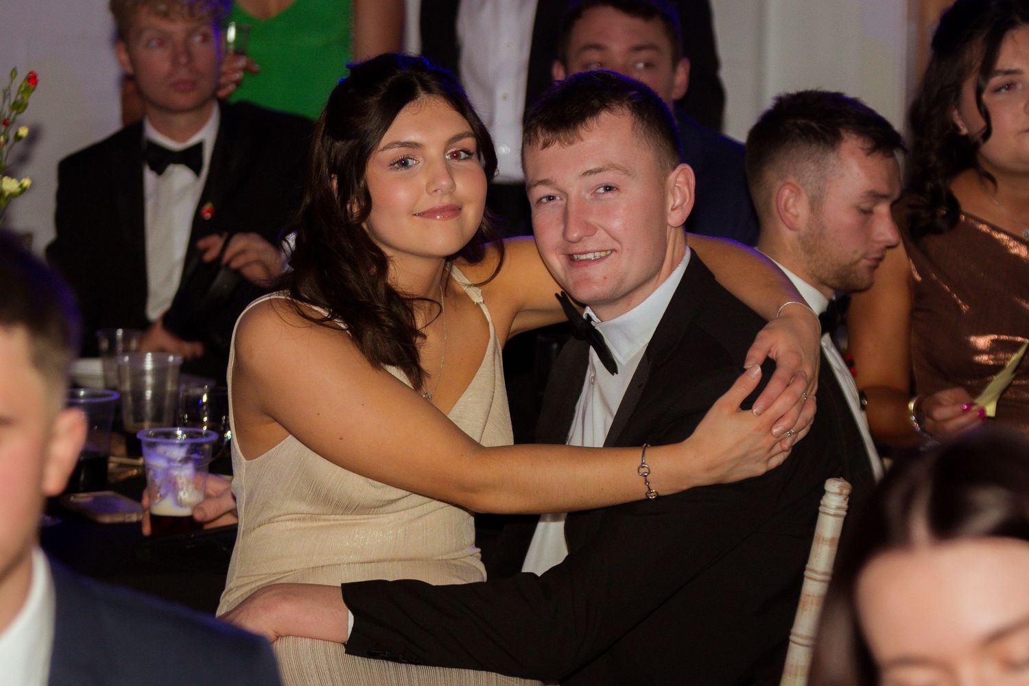 Young couple embracing and smiling at a formal gala dinner event, dressed in elegant attire.