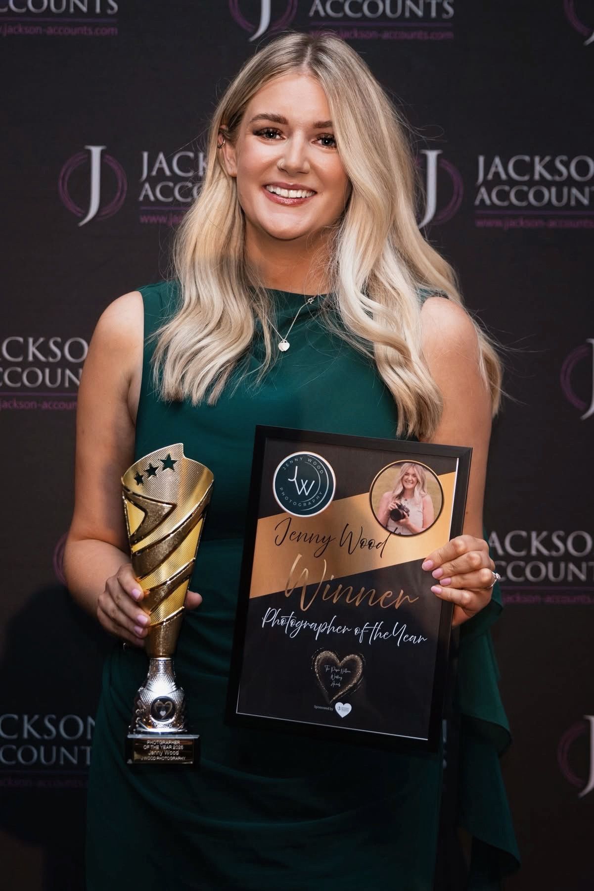 Woman in green dress holds trophy and Photographer of the Year award plaque at Jackson Accounts ceremony.