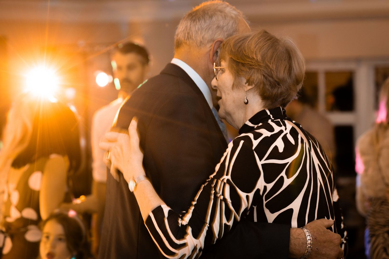 Elderly couple shares romantic dance at wedding reception under warm golden lights.