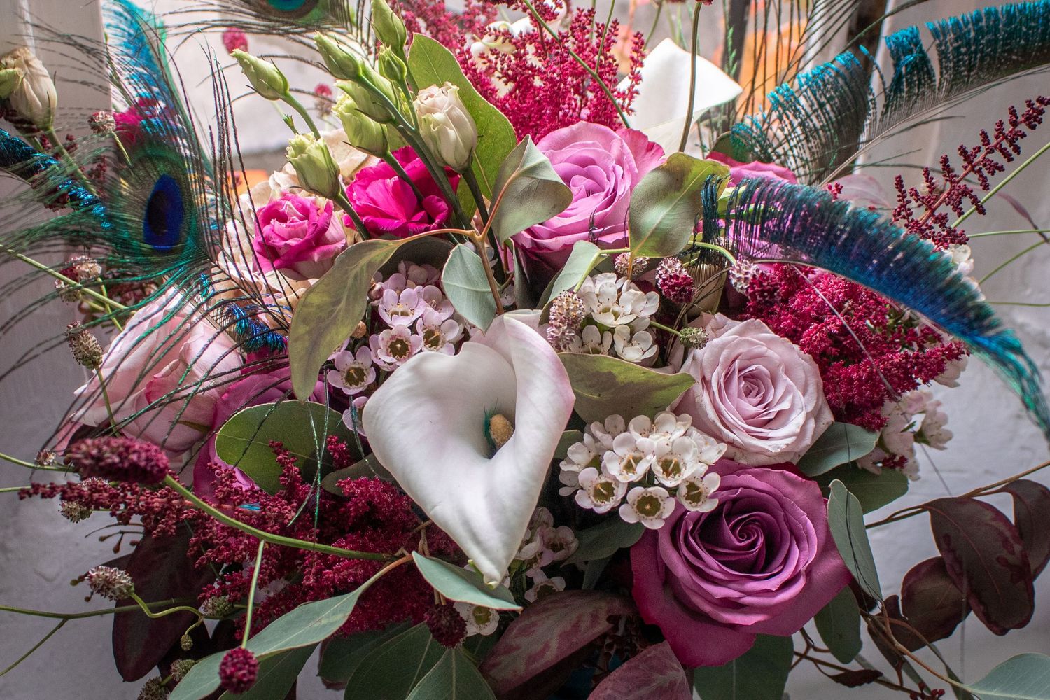 Stunning bridal bouquet featuring calla lilies, pink roses, peacock feathers, and lush greenery.
