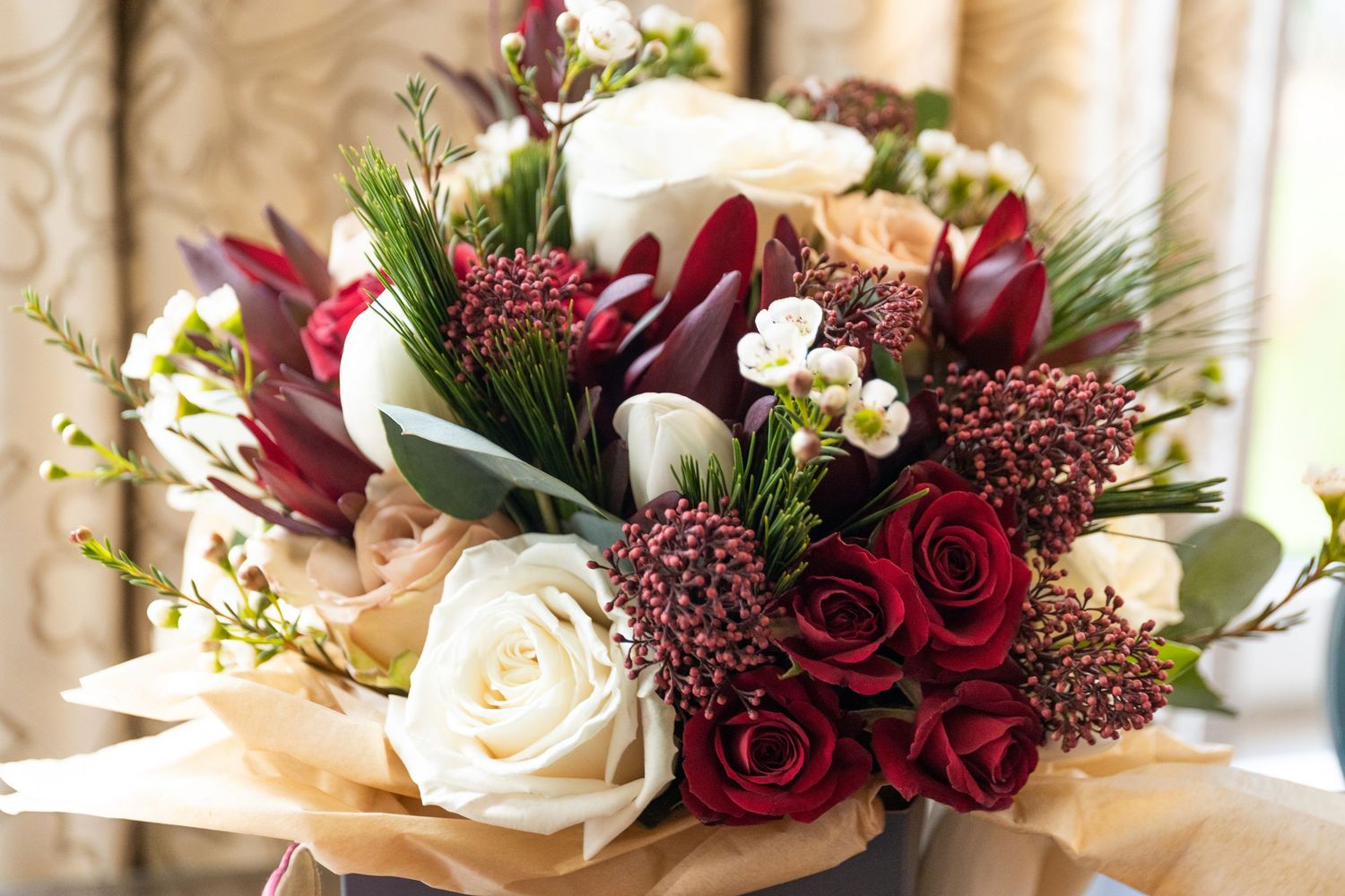 Elegant wedding bouquet featuring red roses, white blooms, and greenery wrapped in brown paper.
