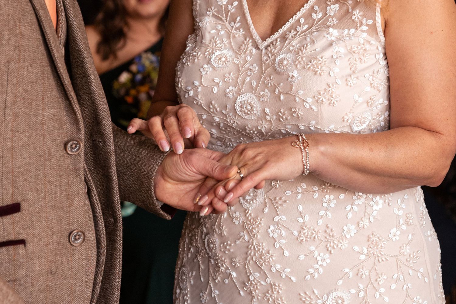 Close-up of couple exchanging rings during wedding ceremony, bride in beaded white gown.
