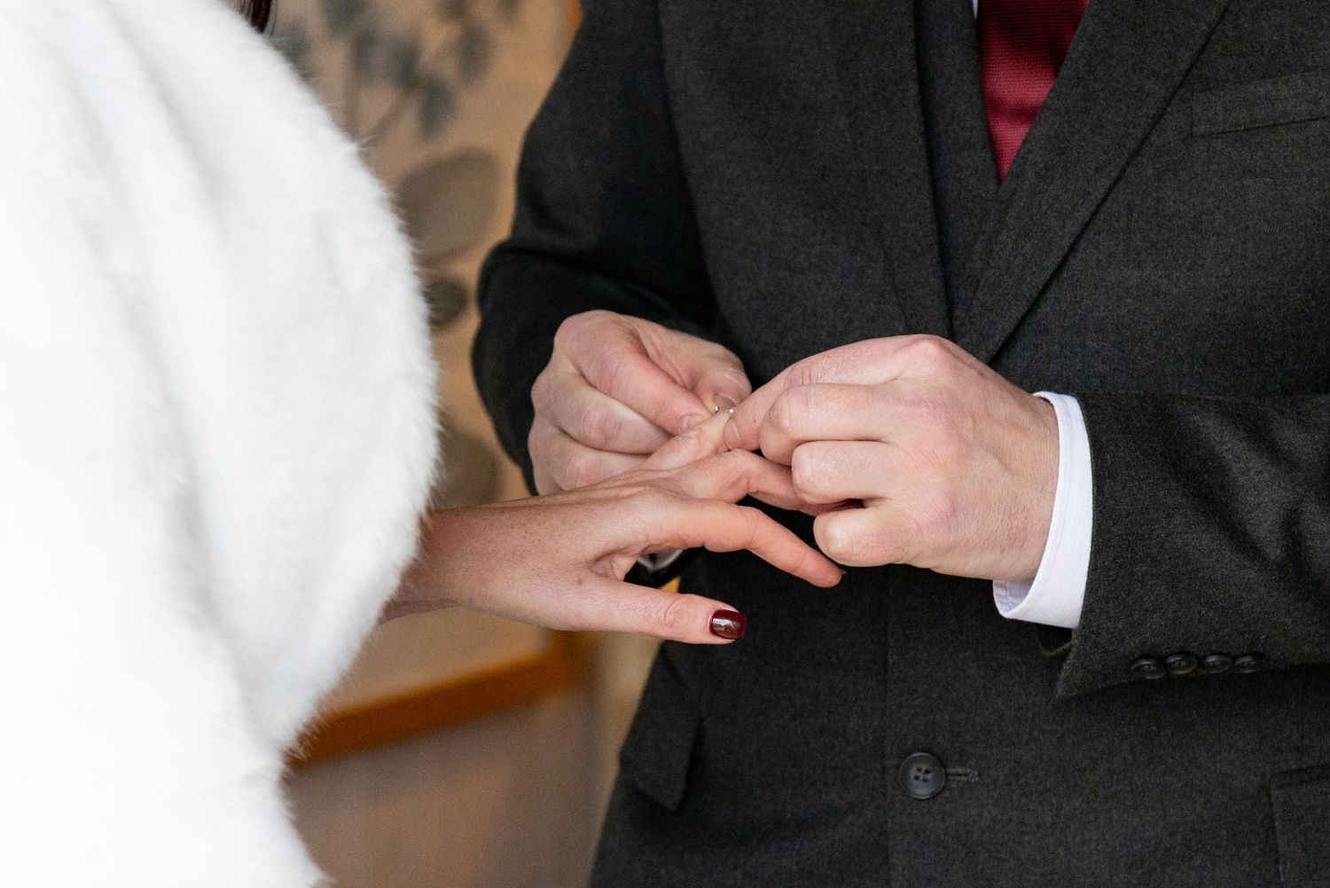 Groom placing a wedding ring on brides finger during ceremony, close-up of hands in elegant attire.