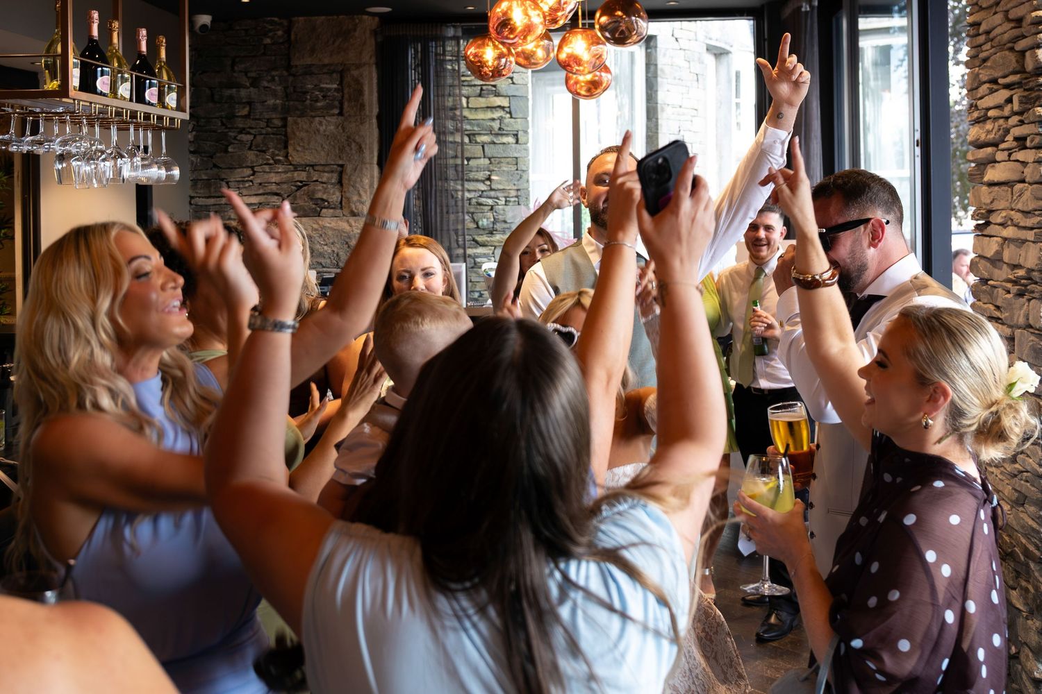 Group of women celebrating at a bar, raising glasses and hands in a lively party atmosphere.