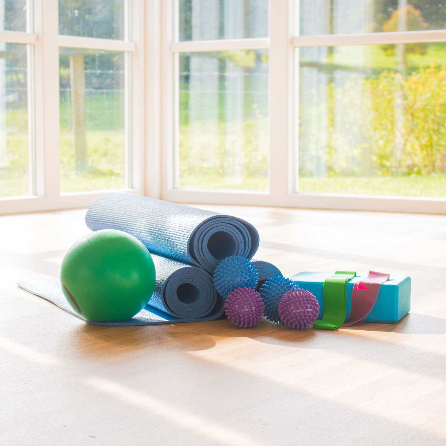 Yoga and Pilates equipment including mats, balls and blocks by a sunny window.