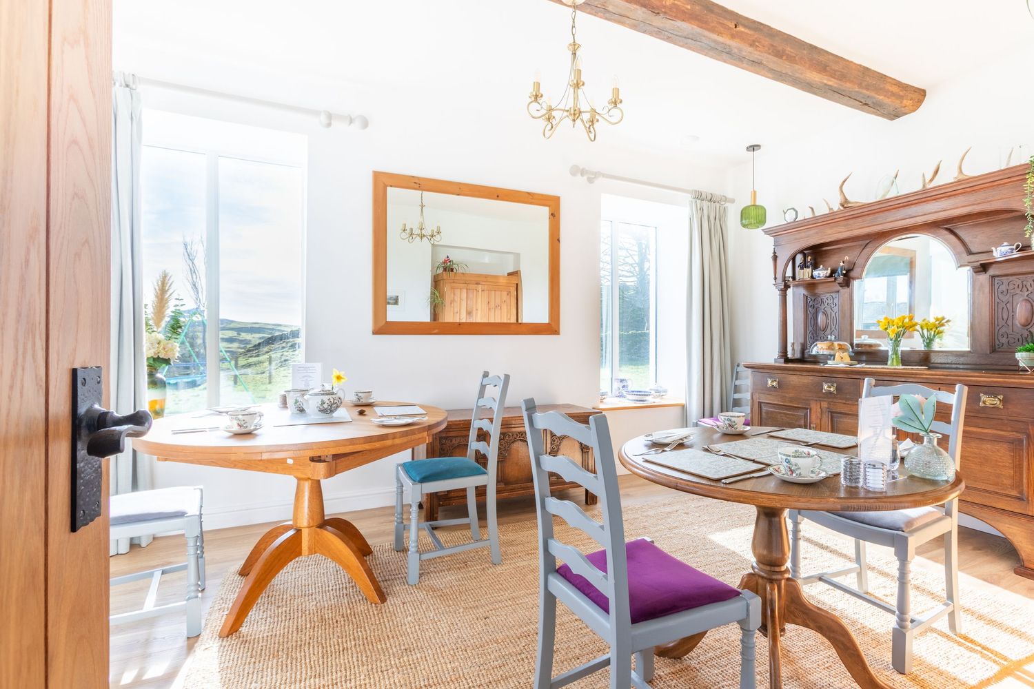Charming dining room with exposed wooden beam, round table, grey chairs, and large windows with countryside views.