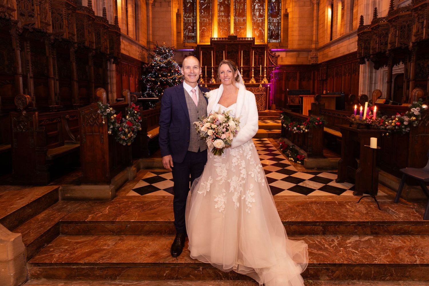 Newlyweds smiling together in stunning decorated church with checkered floor and warm candlelight.