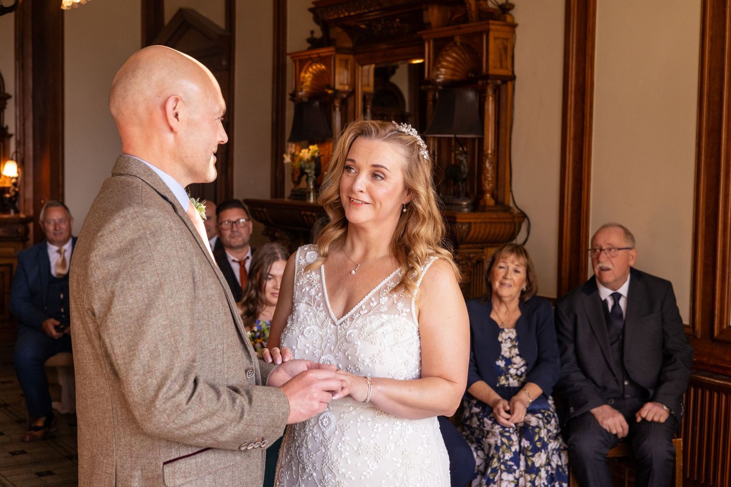Bride and groom exchanging rings during wedding ceremony with guests seated behind.