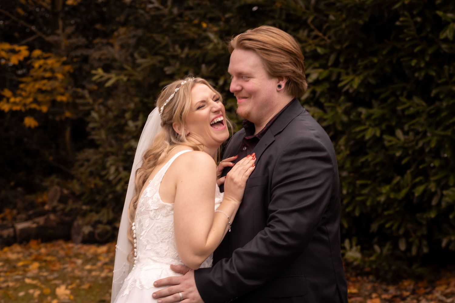 Joyful bride and groom laughing together outdoors among autumn foliage on their wedding day.