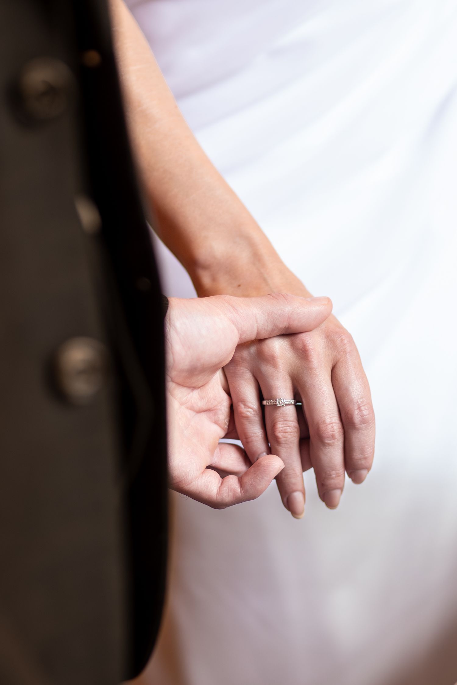 Close-up of two hands with wedding rings, one resting on the other against a white wedding dress backdrop.