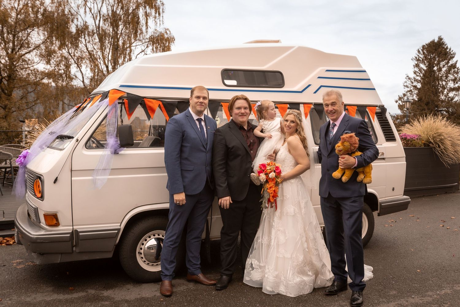 Wedding party posing in front of a decorated vintage VW campervan with orange bunting.