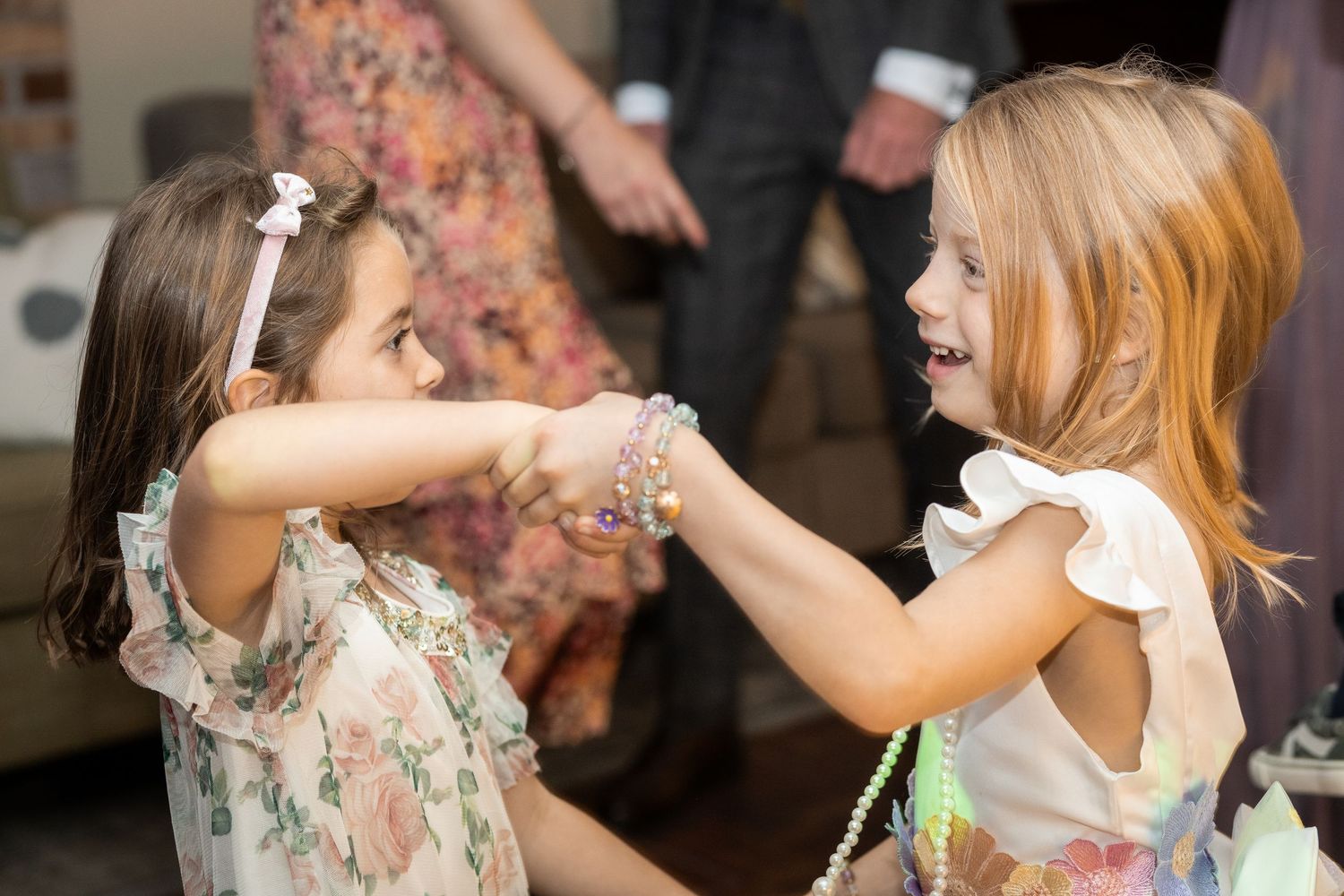 Two young girls in floral dresses joyfully hold hands and dance together at a celebration.