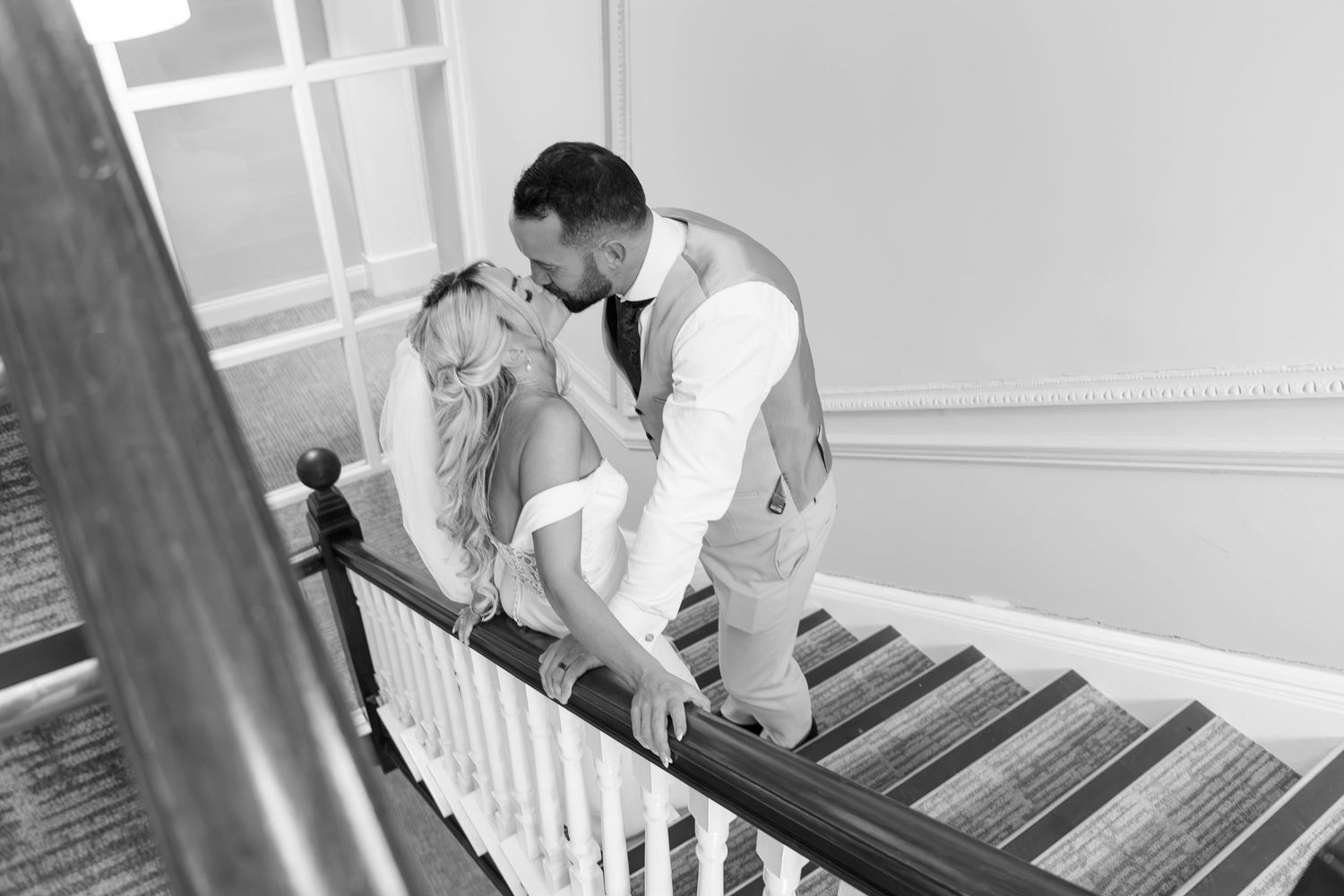 Black and white photo of bride and groom kissing on staircase.