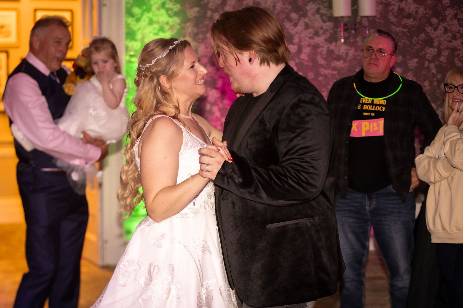 Bride and groom share their first dance at a wedding reception with guests watching in the background.