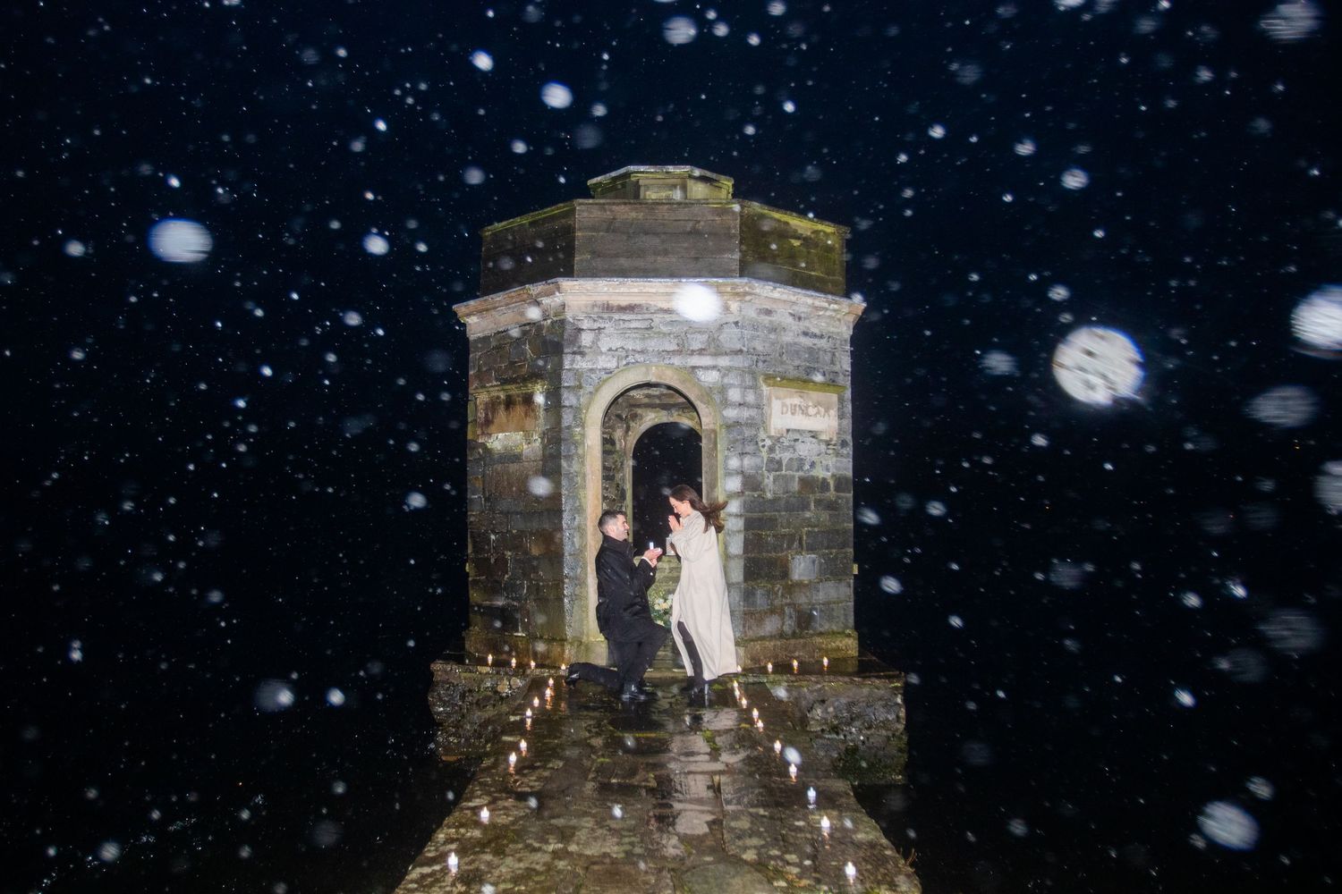 Couple sharing a romantic kiss in a stone tower doorway during a magical snowy night wedding.