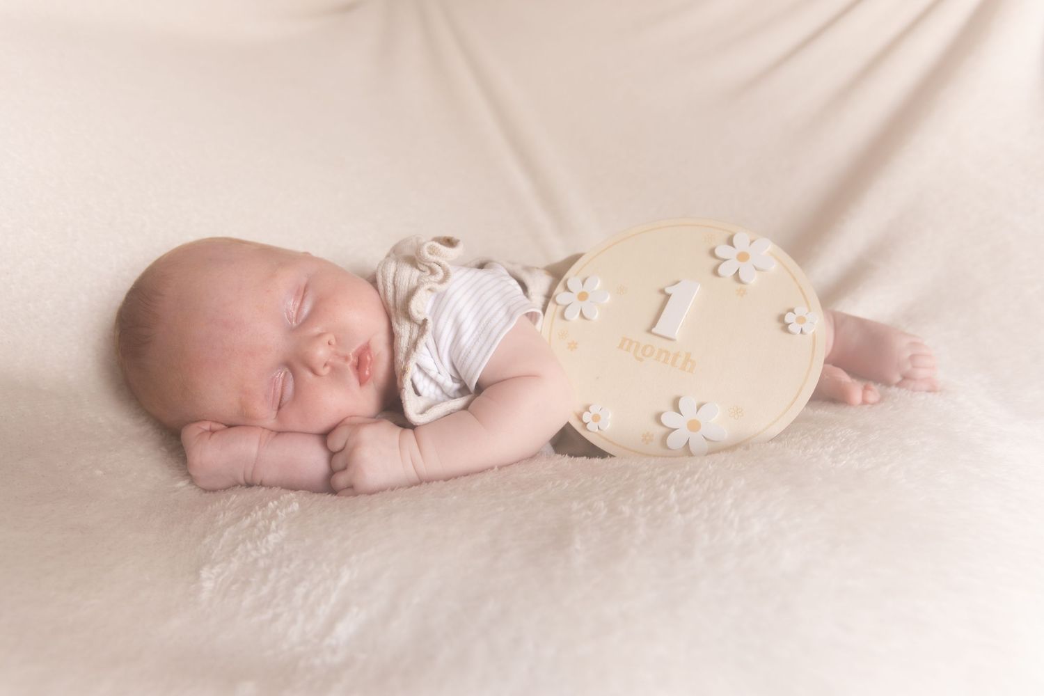 Peaceful newborn baby sleeping on a cream blanket with a number one milestone wooden prop.