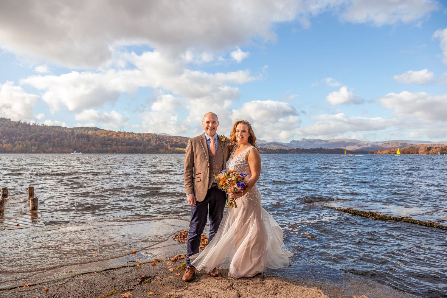 Bride and groom standing by lakeside under dramatic autumn sky.