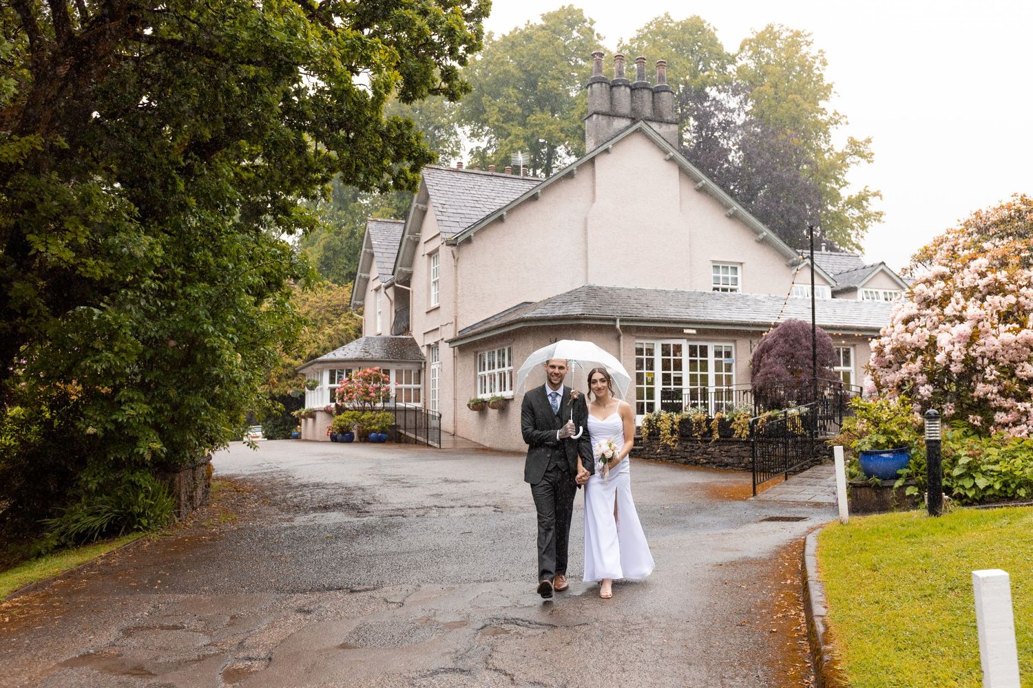 Bride and groom walking hand in hand on a rainy driveway outside an elegant country house wedding venue.