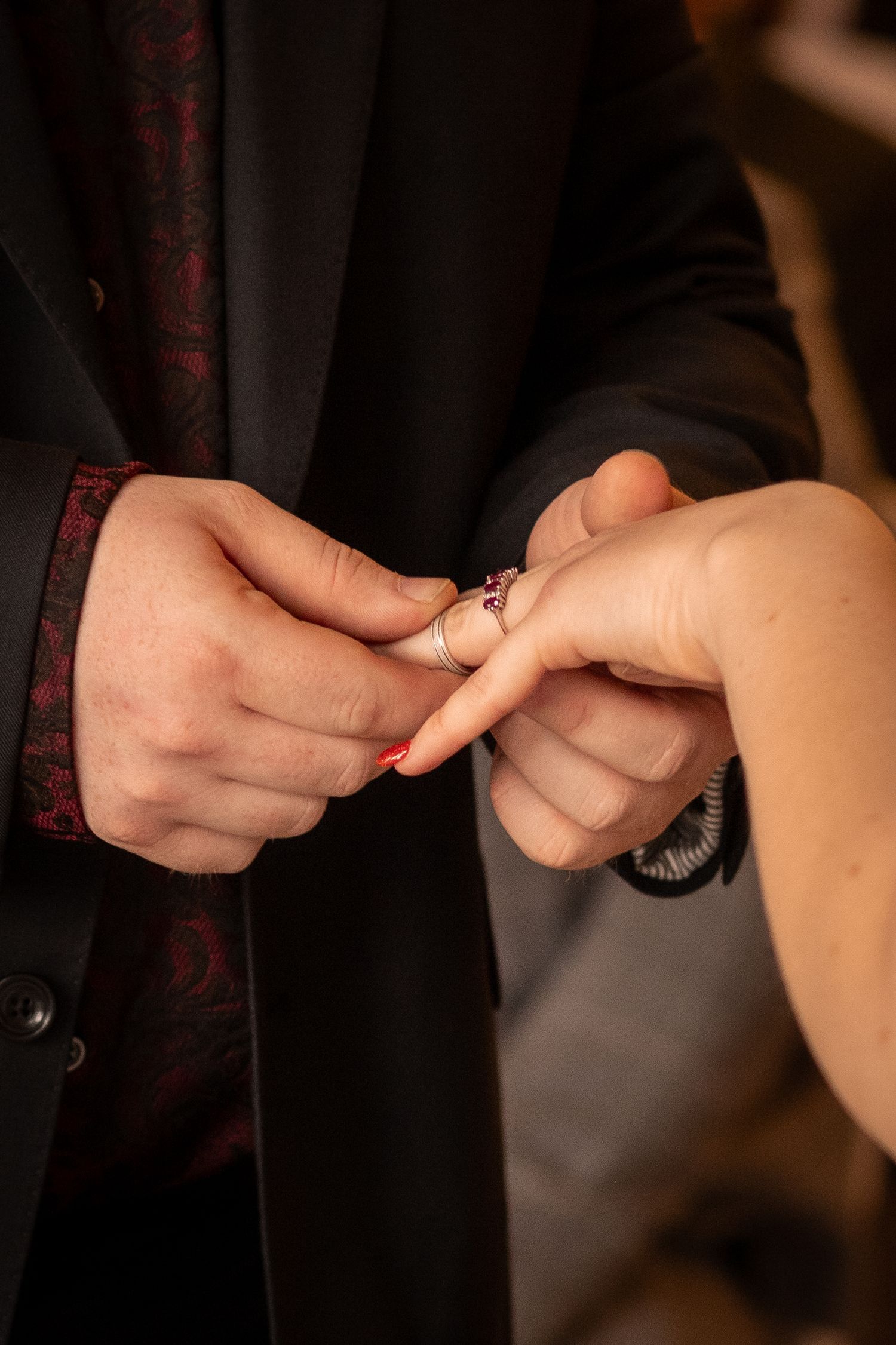 Groom placing a diamond engagement ring on bride's finger during wedding ceremony, close-up of hands.