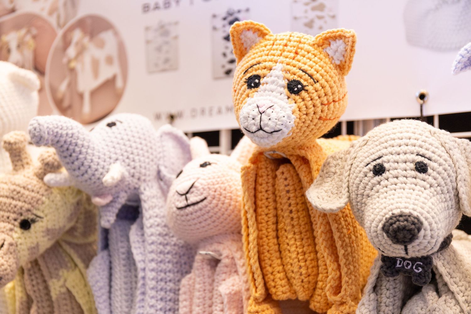 Colorful crocheted animal stuffed toys including a cat, giraffe, and dog at a baby fair.