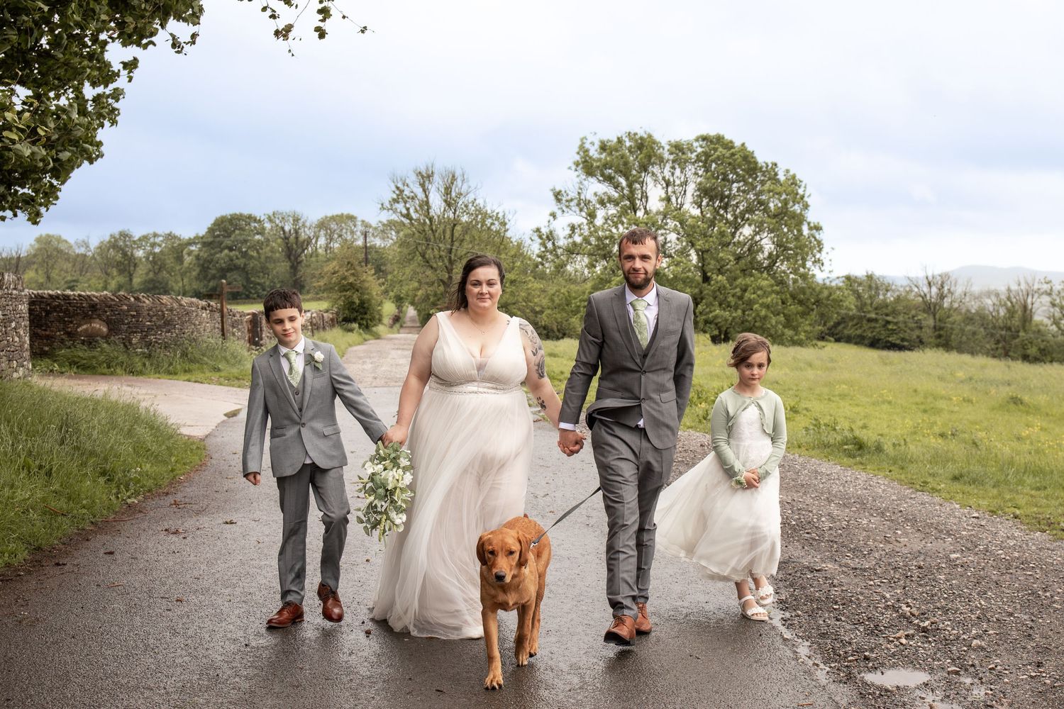 Bride and groom walking with two children and a golden dog on a country road on their wedding day.