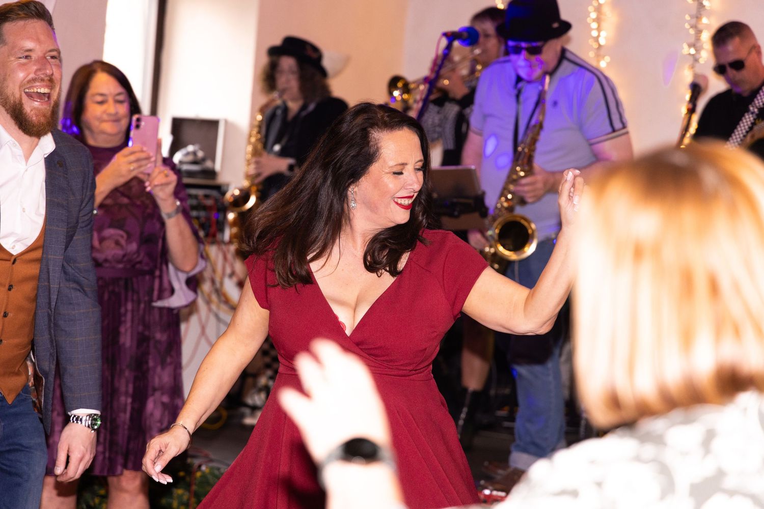 Woman in red dress dancing joyfully at a live band event with musicians playing saxophone in background.