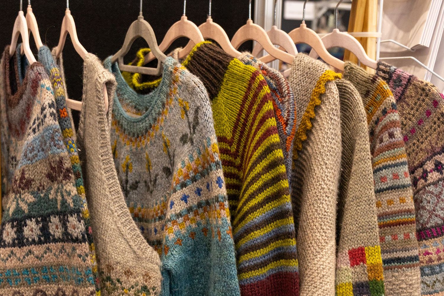 Colorful handknitted fair isle and striped wool sweaters hanging on wooden hangers.