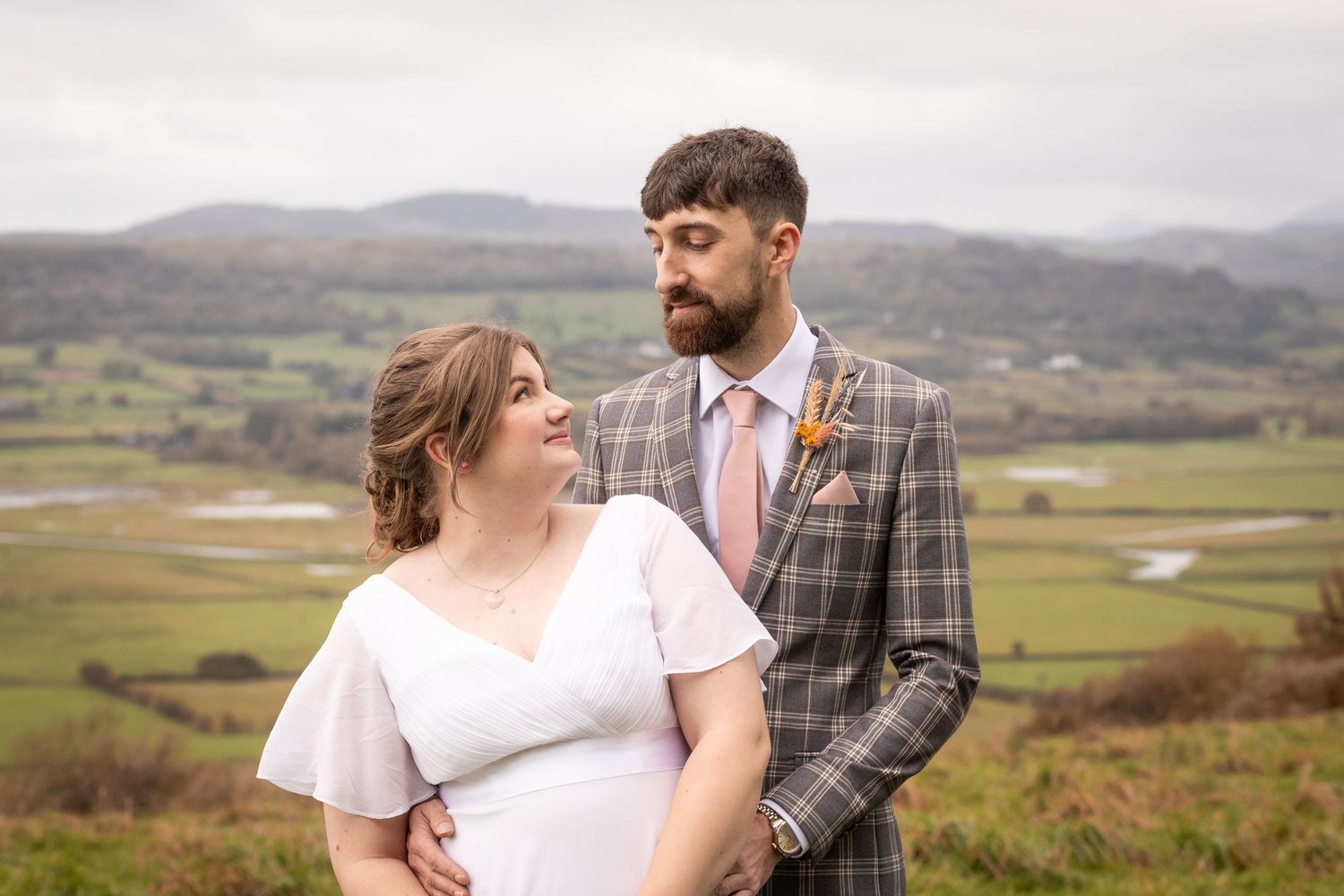 Bride and groom sharing a romantic moment with scenic countryside views behind them.