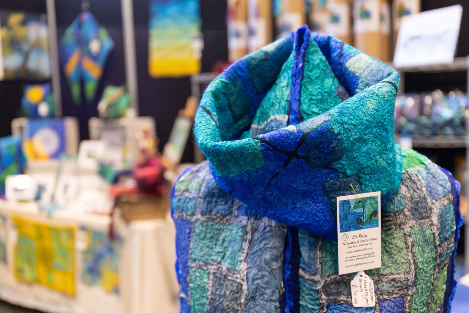 Vibrant blue and teal felted wool scarf displayed on a mannequin at an arts and crafts fair.
