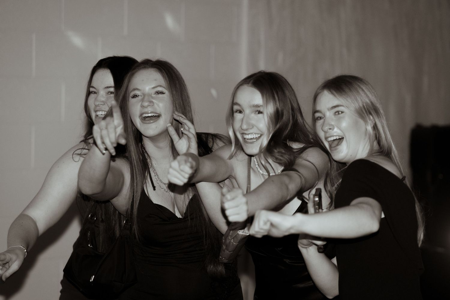 Black and white photo of four young women laughing and dancing together at a party.