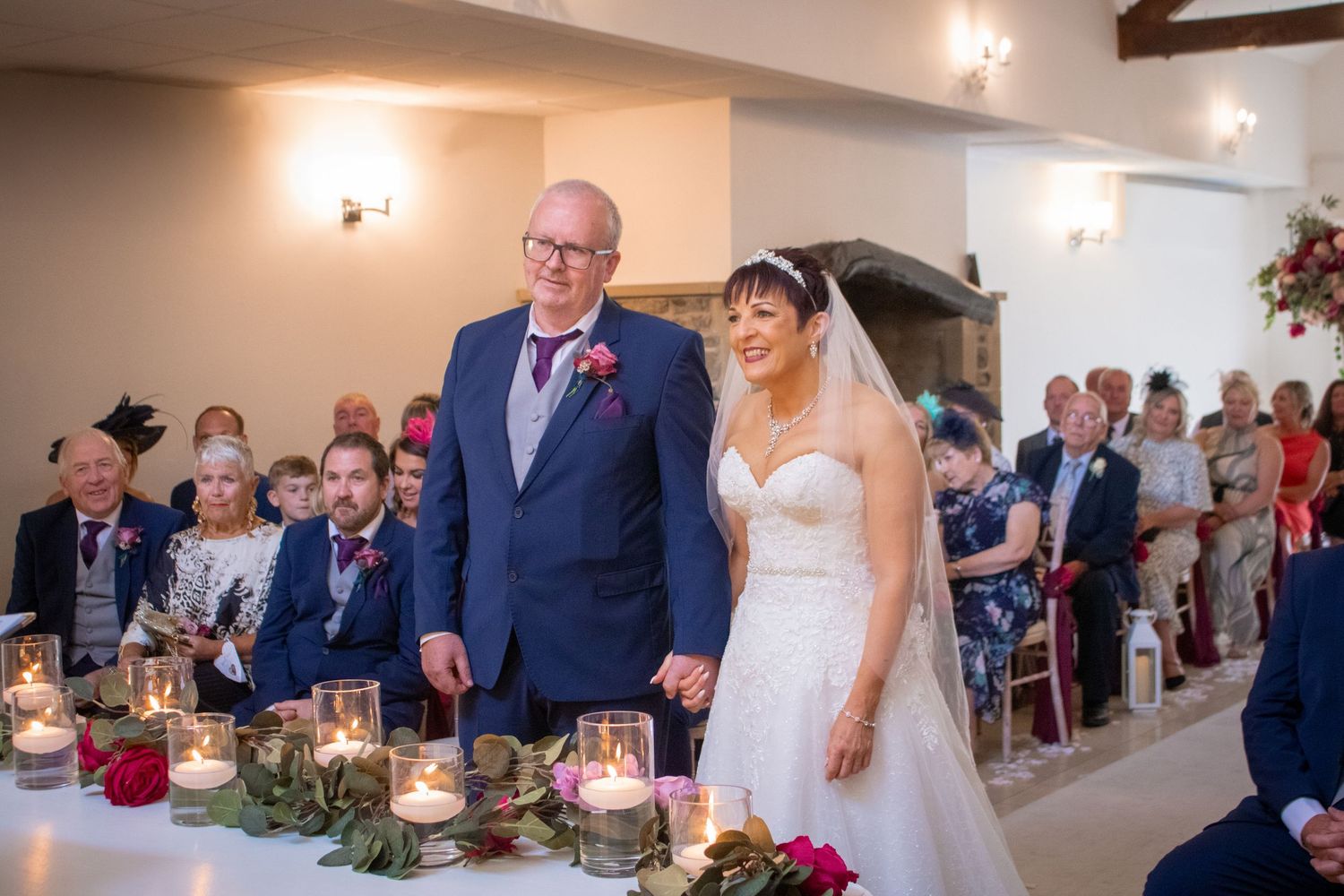 Bride and father walk down the aisle at an elegant wedding ceremony with candles and floral decorations.