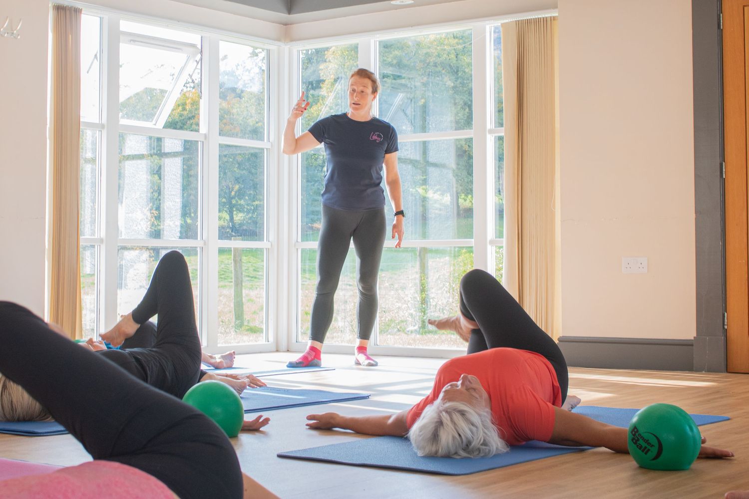 Fitness instructor leading a Pilates class with participants on blue exercise mats.