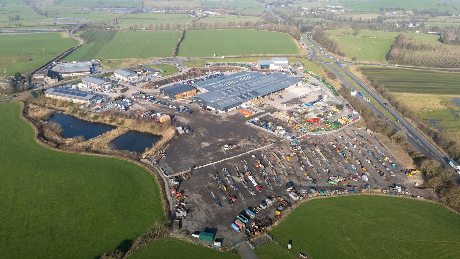 Aerial view of a large commercial industrial complex surrounded by green fields and parking areas.